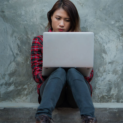 Person sitting against wall accessing media on a laptop