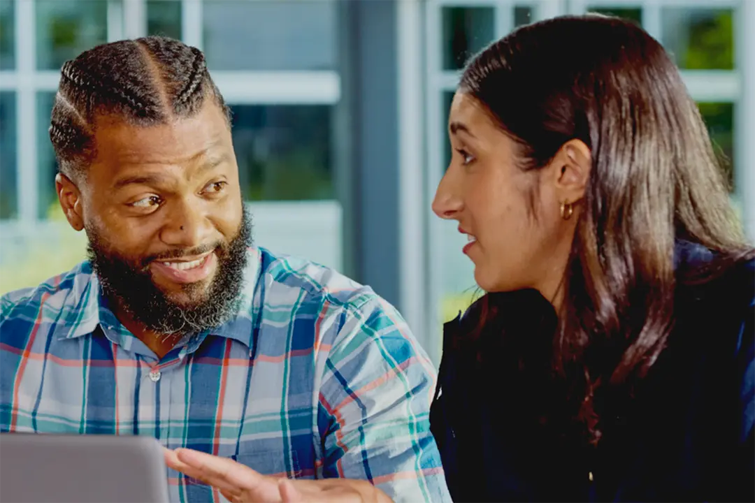 Two adults having a discussion in front of a laptop computer