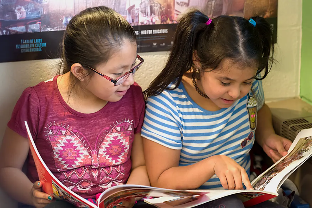 Two school aged children sitting together and reading books