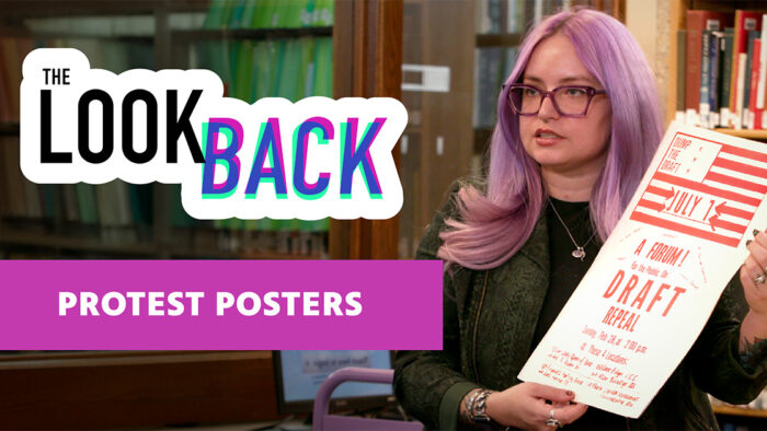Woman with purple hair holding a “Dump the Draft” flyer beside a sign reading “THE LOOK BACK” and text “PROTEST POSTERS” on a purple banner.