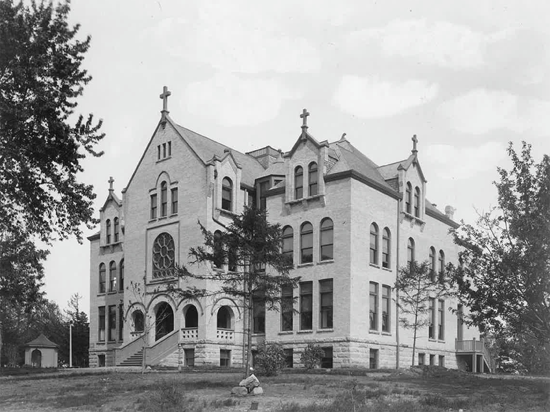 A black and white photograph of a large brick building with many arched windows and a stone foundation.