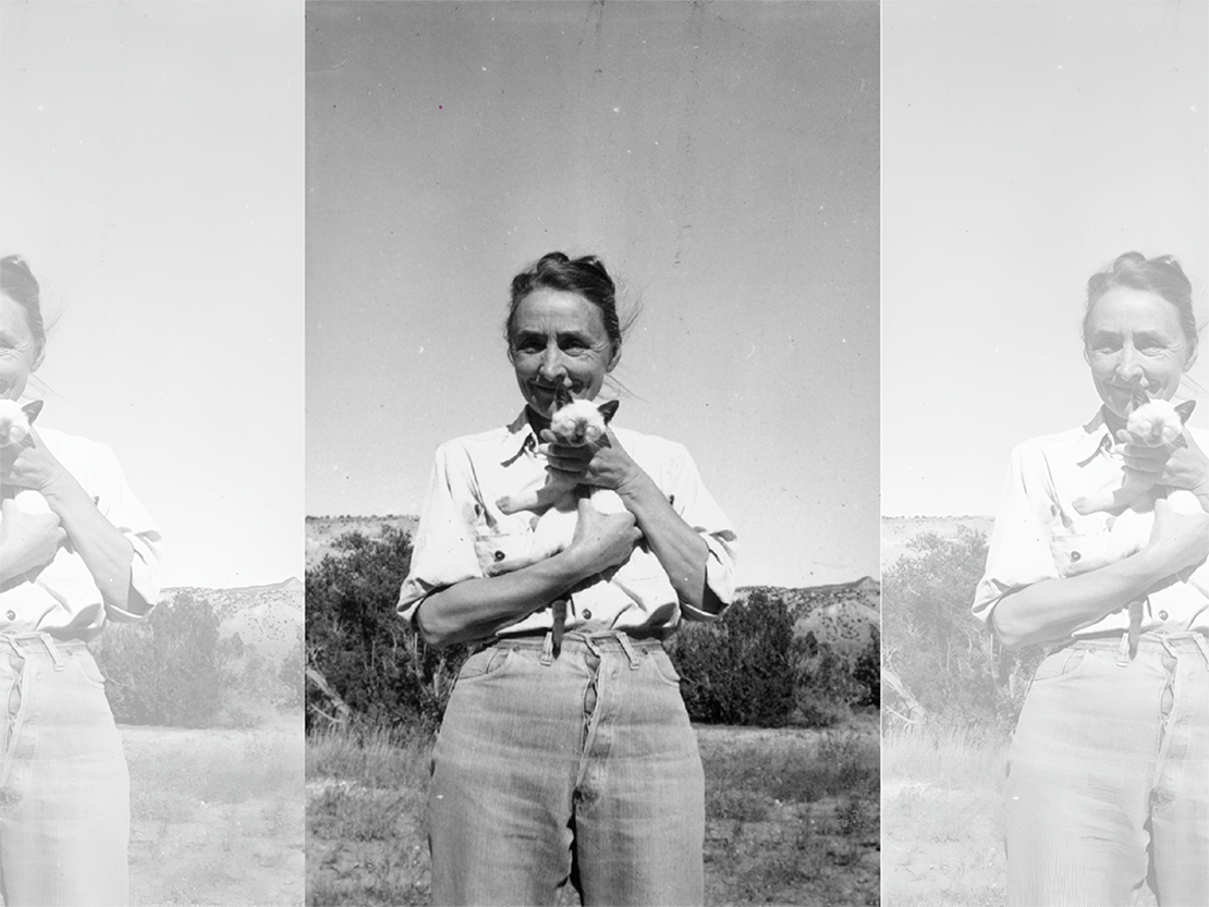 A black and white photograph of Georgia standing outside in jeans and a shirt with the sleeves rolled up. She is holding a small cat.