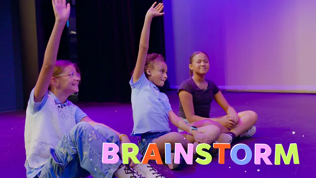Students learning Whoopensocker, sitting on the floor with hands raised, with text superimposed, BRAINSTORM