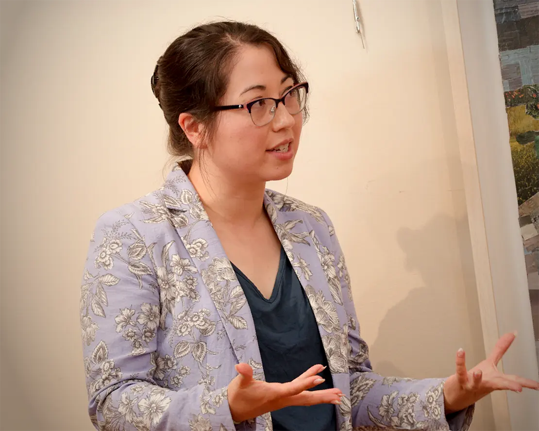 Woman in a floral-patterned blazer gesturing while speaking indoors.