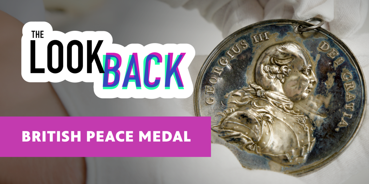 A close-up of a silver British peace medal depicting King George III in profile, held with white gloves. Text overlay reads “The Look Back” and “British Peace Medal.”