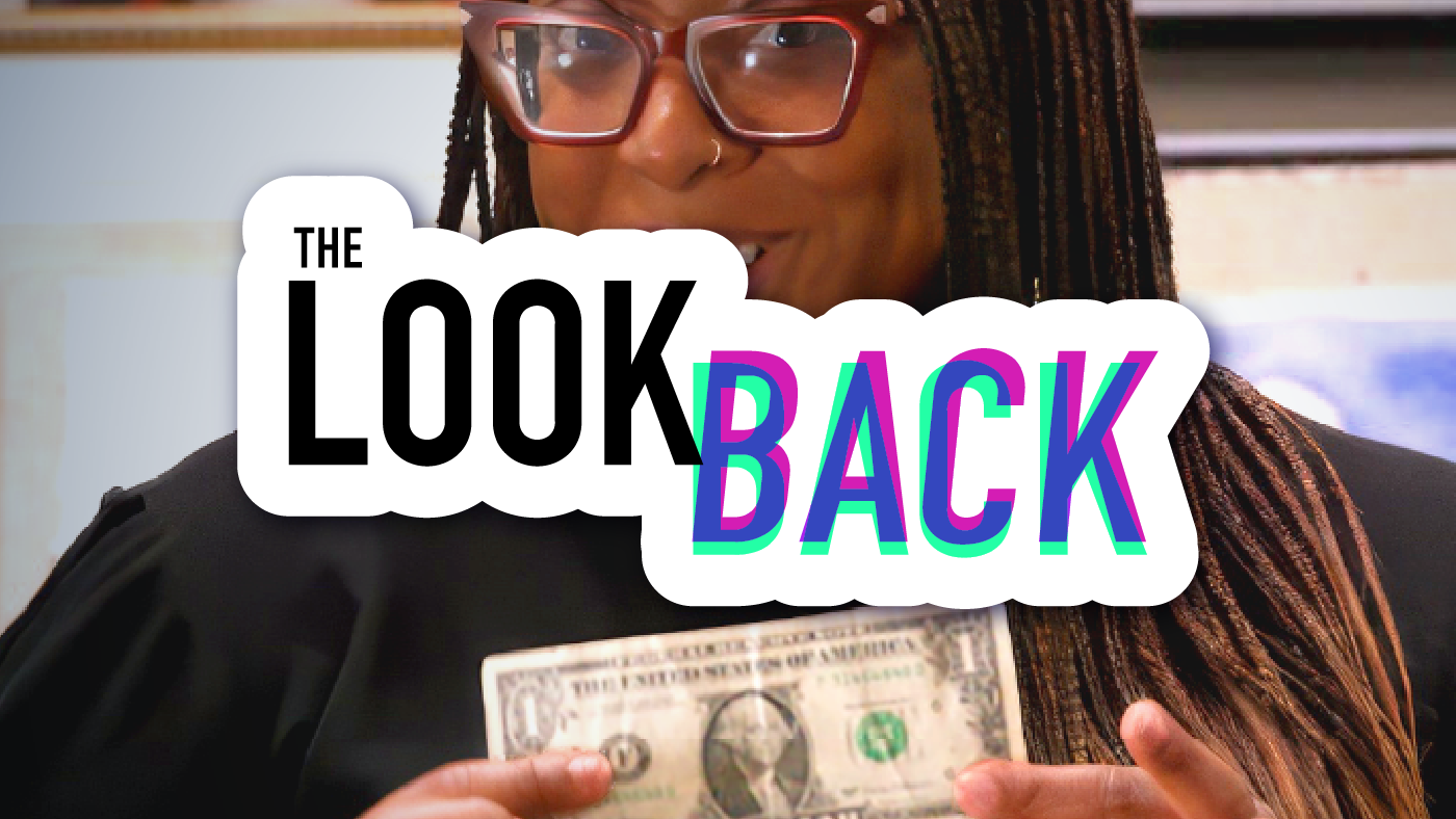 Host of the show holding a one-dollar bill with the logo for “The Look Back” superimposed