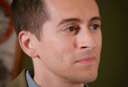 Close-up of man with short dark hair in a neutral expression, facing slightly right.