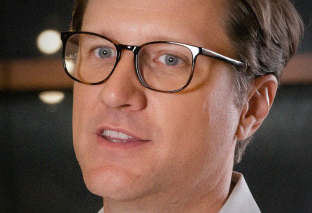 Close-up of man with short dark hair in a neutral expression, facing slightly right.