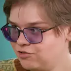 Person with dark-rimmed glasses and light brown hair in a white shirt, looking slightly to the side.