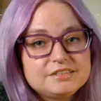 Person with short hair wearing purple glasses and a patterned sweater, looking slightly left.