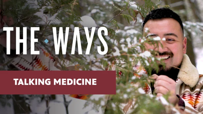 Promotional graphic for "Talking Medicine," an episode of The Ways. A smiling young man with a beard peers through snow-dusted evergreen branches, wearing a patterned blanket coat. Bold white text reads "THE WAYS" and a dark red banner reads "TALKING MEDICINE."