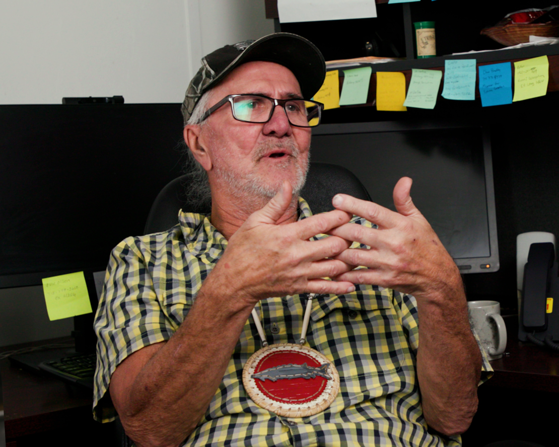 Person wearing a camouflage cap and glasses speaking to camera in an office setting