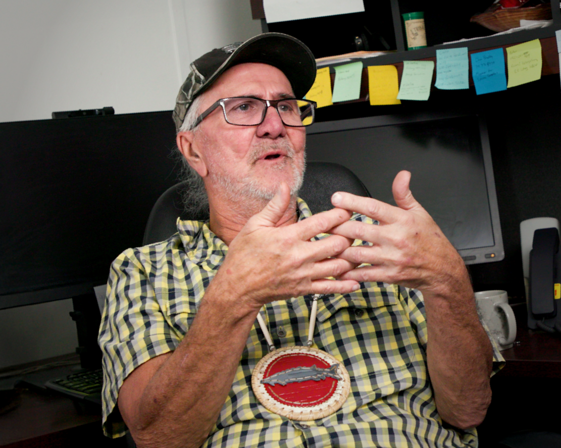 Person wearing a camouflage cap and glasses speaking to camera in an office setting