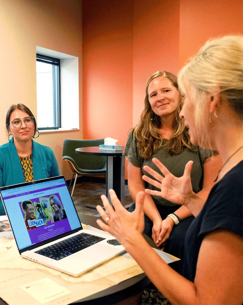 Three adults gathered around a laptop and having a discussion