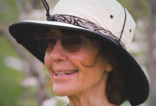 Headshot of Deirdre, smiling, wearing a wide-brimmed sun hat and sunglasses, photographed outdoors.