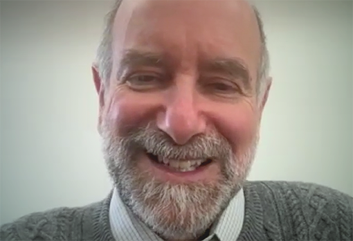 Jonathan Patz laughs broadly during a video interview, wearing a gray cable-knit sweater against a light background.