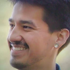 Portrait of Ray Allen smiling in profile, with short dark hair and a small gauge earring, set against a soft green outdoor background.