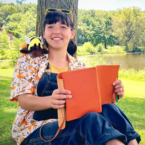 Ami Eckard-Lee, host of Field Notes on Climate, leaning up against a tree on a sunny day