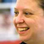 Person with pulled-back hair laughing in profile with colorful blurred background