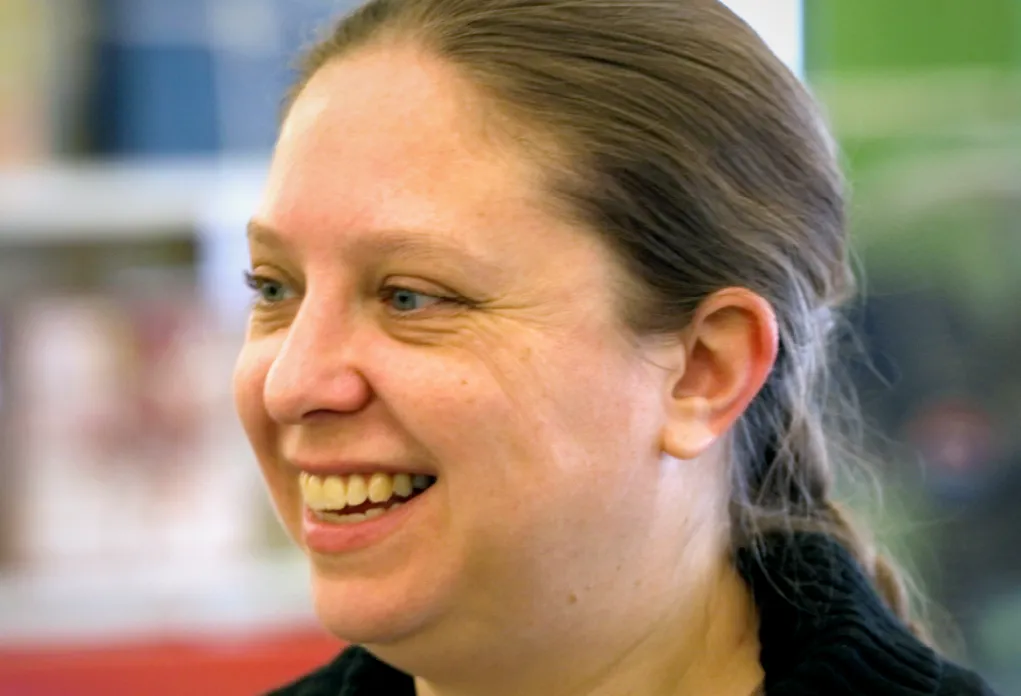 Person with pulled-back hair laughing in profile with colorful blurred background