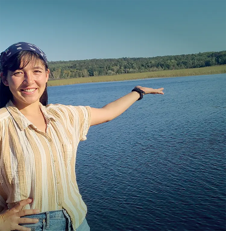 Ami Eckard-Lee, host of Field Notes on Climate, standing in front of a lake on a sunny day