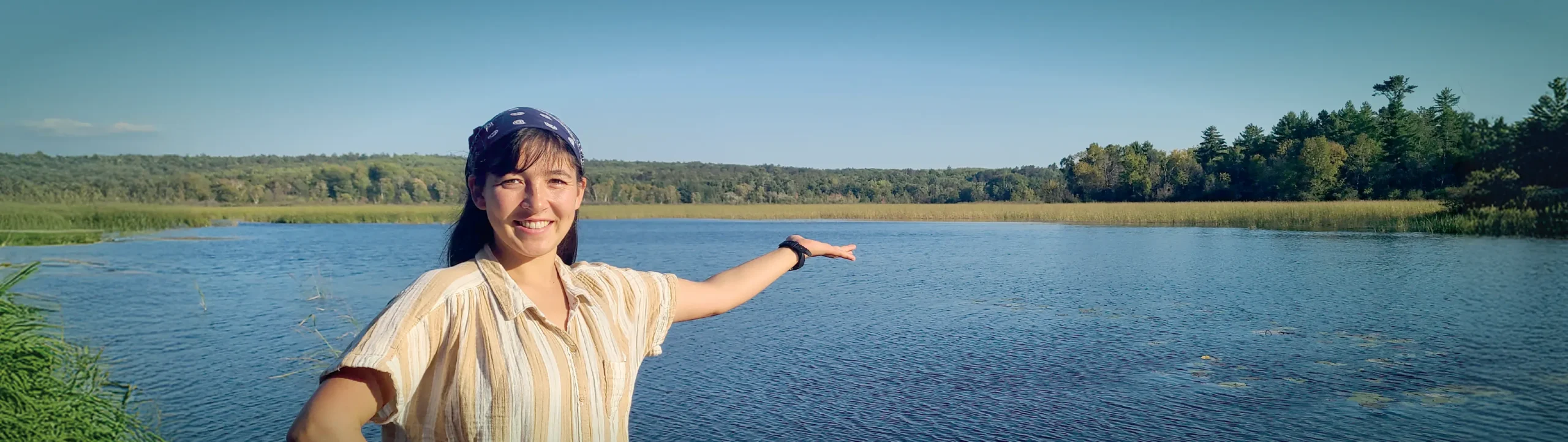 Ami Eckard-Lee, host of Field Notes on Climate, standing in front of a lake on a sunny day