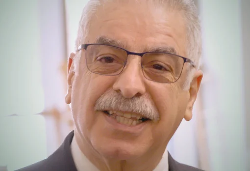 Headshot of guest Majid Sarmadi. They are smiling warmly at the camera, with short white hair, a grey mustache, and thin-framed glasses, wearing a suit jacket, photographed indoors with a soft light background.