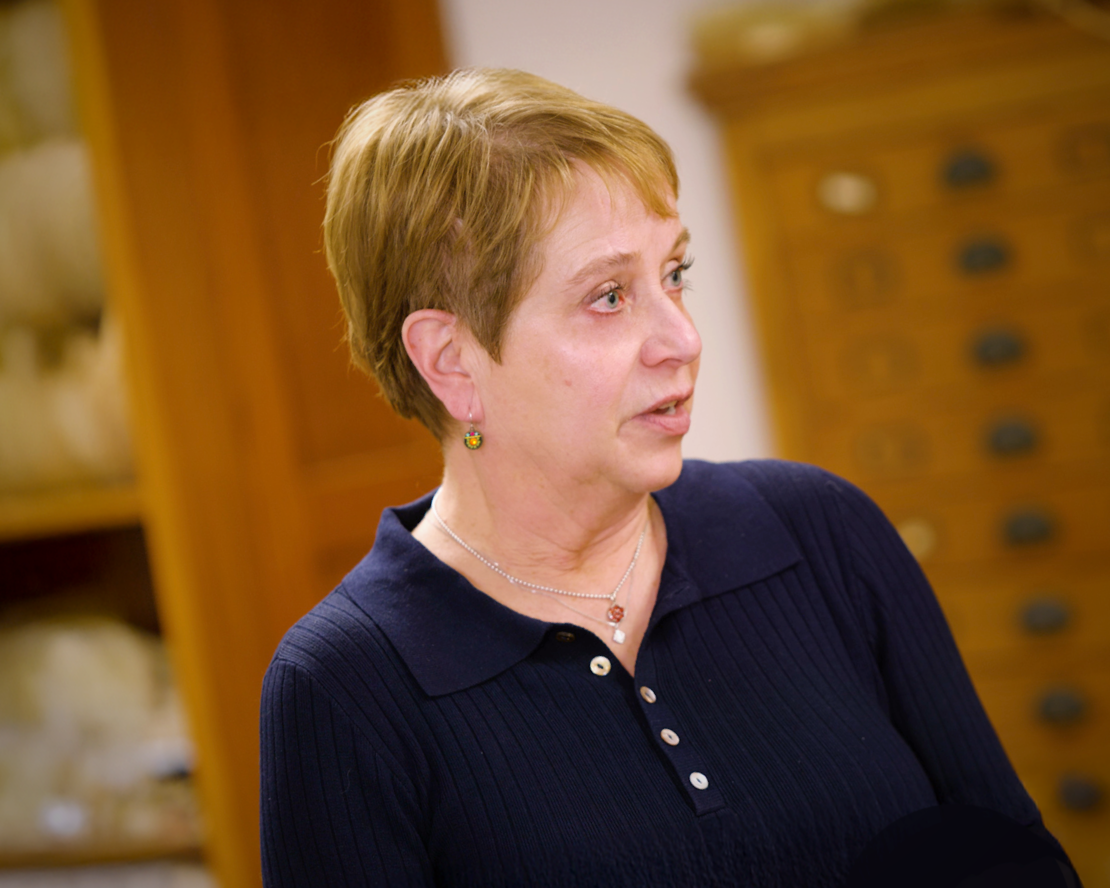 Person in dark sweater stands in an archival room with wooden cabinets of stone artifacts behind them.