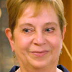 Person with short blond hair smiles slightly, with shelving of artifacts visible behind them.
