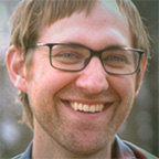 Headshot of Chris Wilson, a smiling man with short brown hair, glasses, and a beard, wearing a gray shirt.
