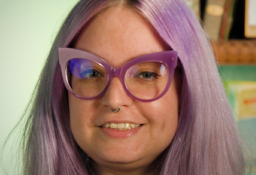 Smiling person with lavender hair and purple cat-eye glasses.