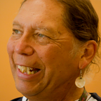 Person laughing, wearing a round shell earring.
