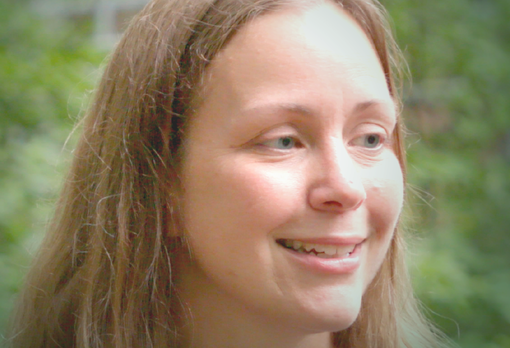 Smiling person with wavy strawberry-blond hair, looking off to the side, indoors.
